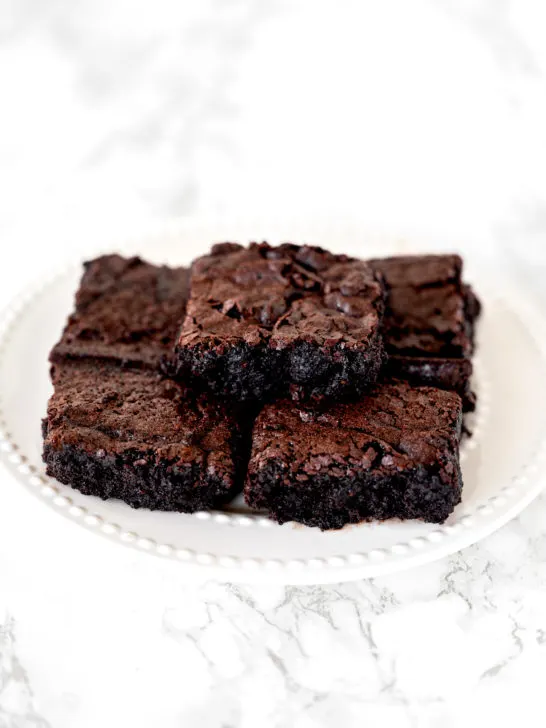 Dairy free brownies piled on a white plate sitting on a white marble counter