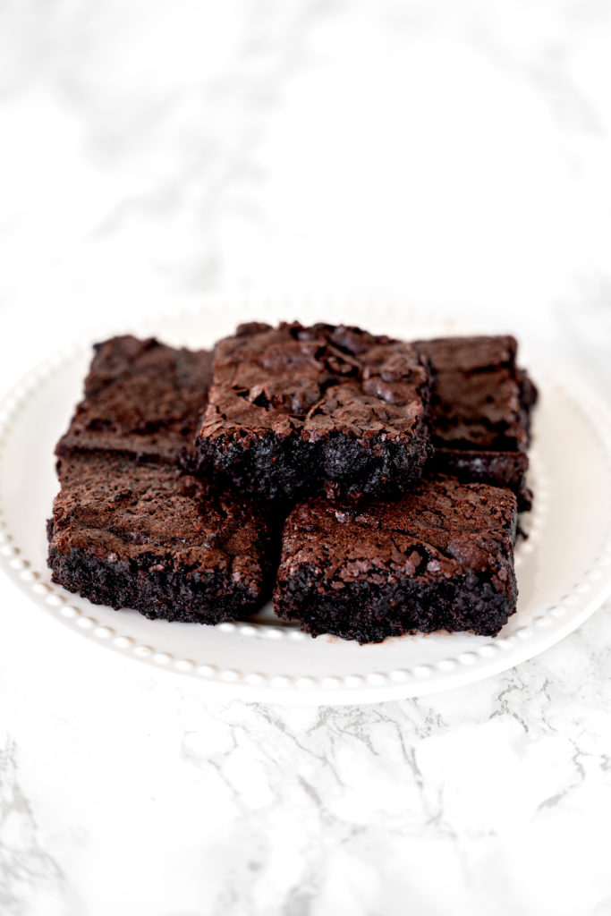Dairy free brownies piled on a white plate sitting on a white marble counter