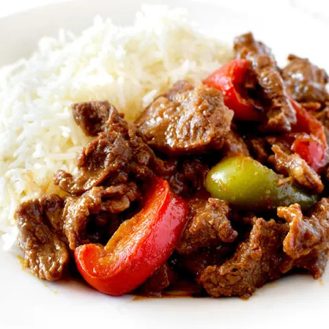 pepper steak and rice on a white plate on a white marble counter