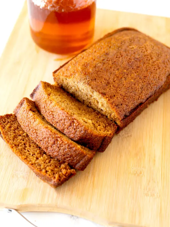 Jewish honey cake on a cutting board with honey in the background