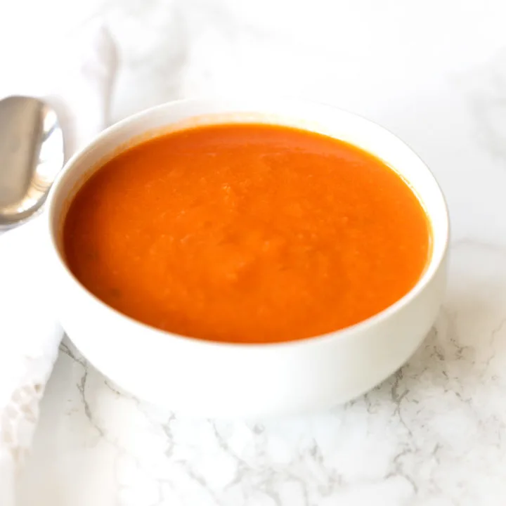 Dairy free tomato soup in a white bowl on a white marble counter