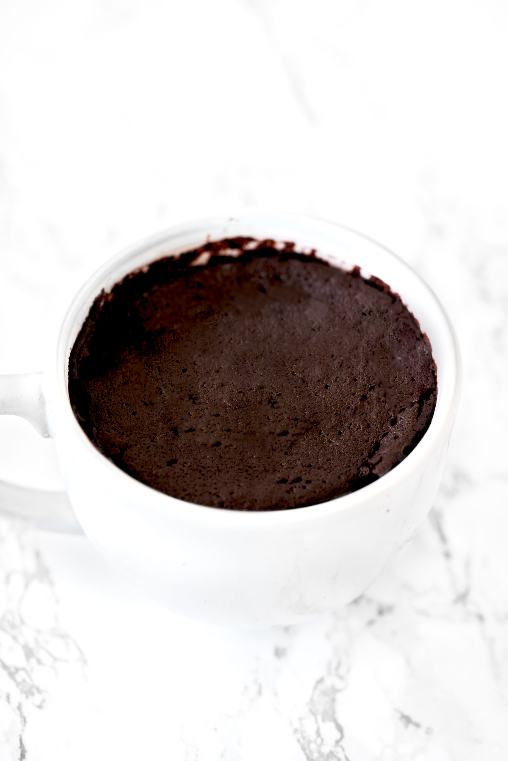 oat flour chocolate mug cake in a white mug on a white marble counter