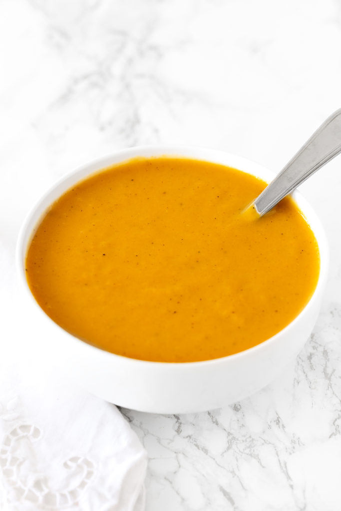 dairy free pumpkin soup in a white bowl on a white marble counter