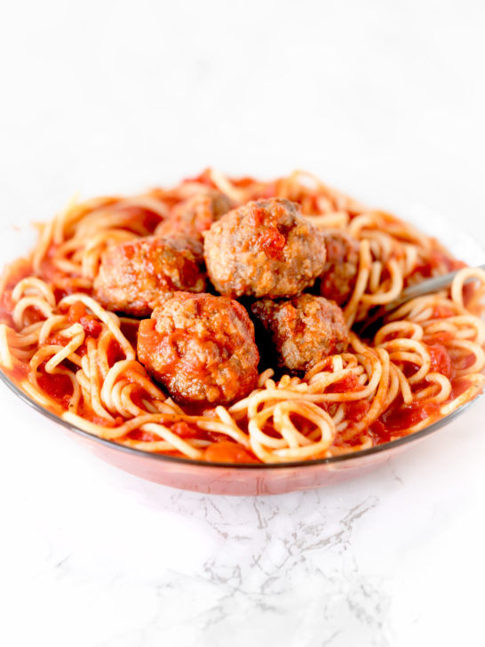 meatballs in a bowl of spaghetti on a white marble counter