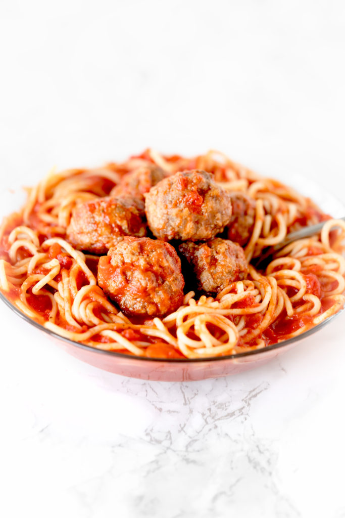 eggless meatballs in a bowl of spaghetti on a white marble counter