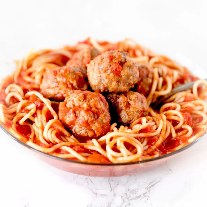 meatballs in a bowl of spaghetti on a white marble counter