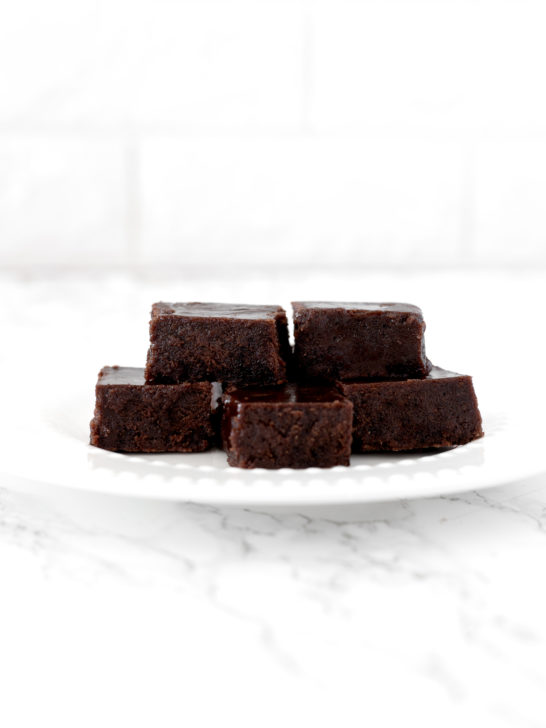 dairy free fudge pieces piled on a white plate on a white marble counter